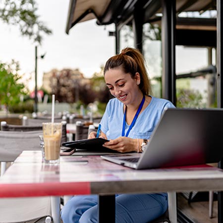 Young female nurse at a table outside looking at her laptop