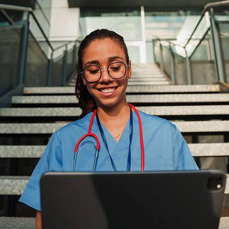 Young female nurse on a laptop sitting on stairs outside